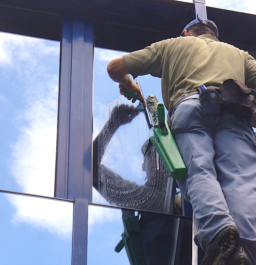 professioneller-Fensterputzer-reinigt-reflektierende-Fenster-auf-einer-Leiter-in-fürth